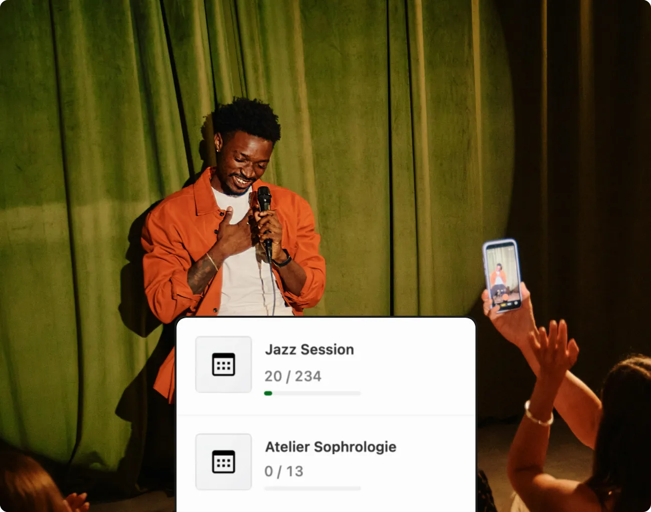 A comedian on stage filmed by the audience, above the HappenBoard list of events with the tickets sold for each